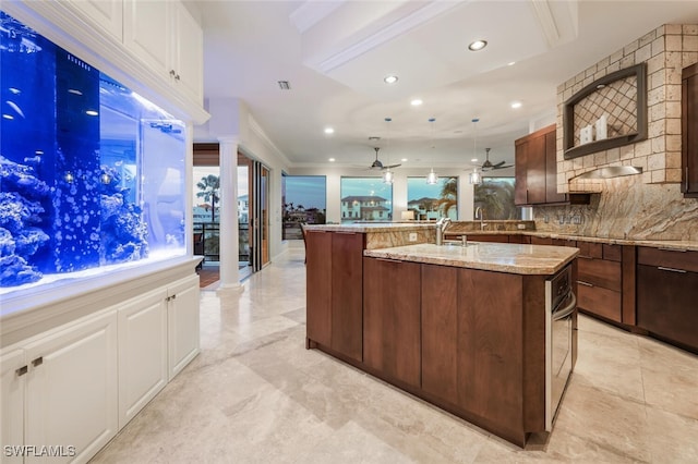 kitchen with an island with sink, decorative light fixtures, ornamental molding, white cabinets, and light stone counters