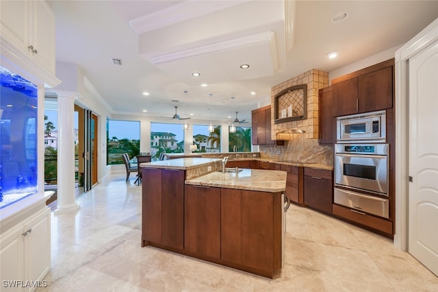 kitchen featuring light stone countertops, stainless steel appliances, tasteful backsplash, ornamental molding, and a kitchen island with sink