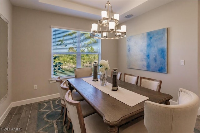 dining room featuring dark wood-type flooring, a raised ceiling, and a chandelier