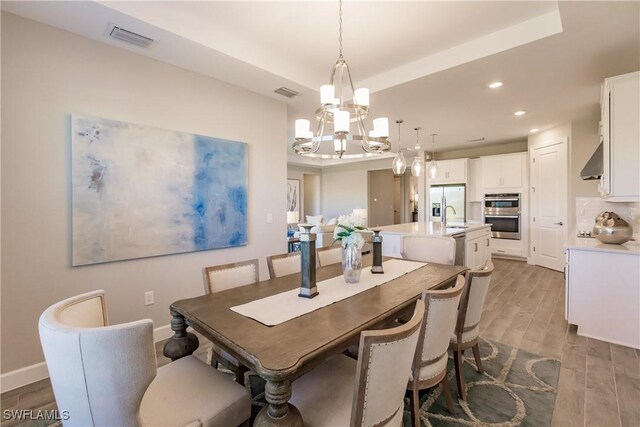 dining room with sink, a raised ceiling, light hardwood / wood-style floors, and an inviting chandelier