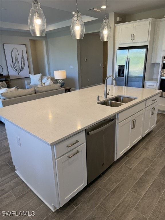 kitchen with a center island with sink, appliances with stainless steel finishes, white cabinets, decorative light fixtures, and sink