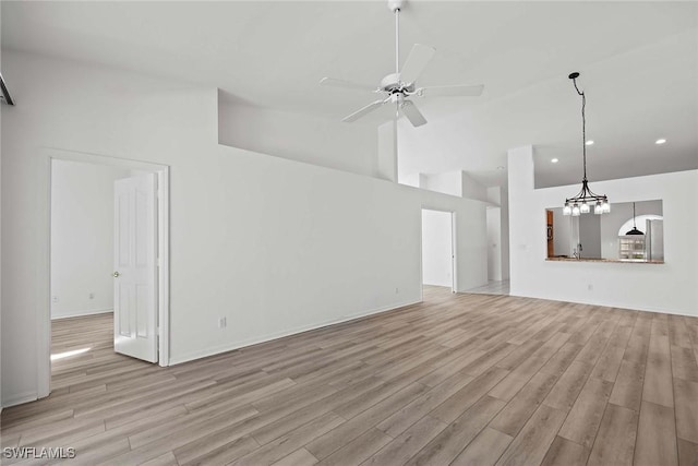 unfurnished living room featuring ceiling fan with notable chandelier, high vaulted ceiling, and light wood-type flooring