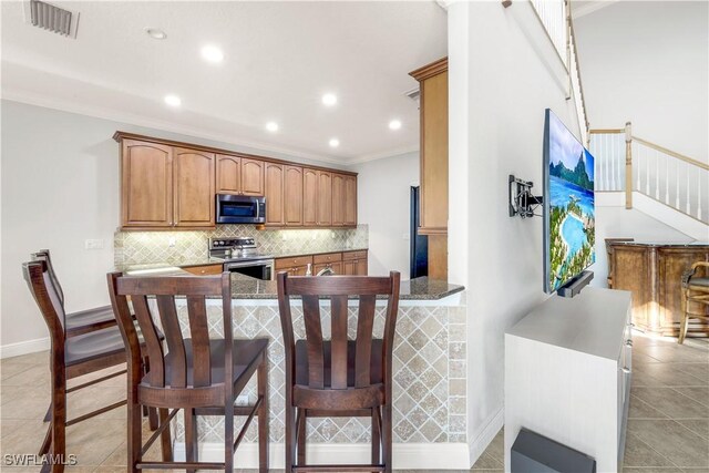 kitchen with backsplash, light tile patterned floors, ornamental molding, appliances with stainless steel finishes, and kitchen peninsula