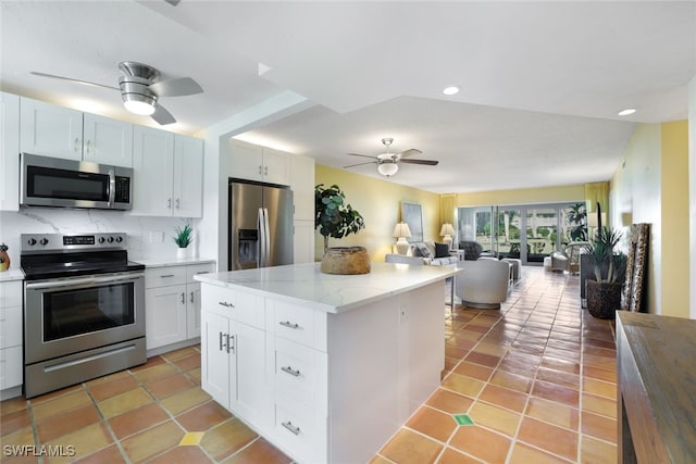 kitchen with appliances with stainless steel finishes, backsplash, light stone counters, white cabinets, and a kitchen island