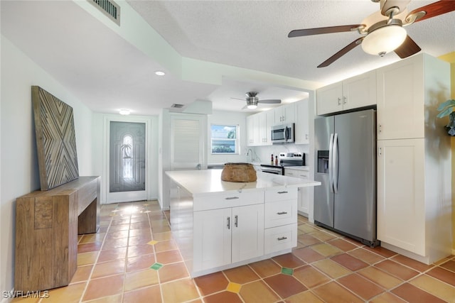 kitchen featuring a textured ceiling, stainless steel appliances, ceiling fan, a center island, and white cabinetry