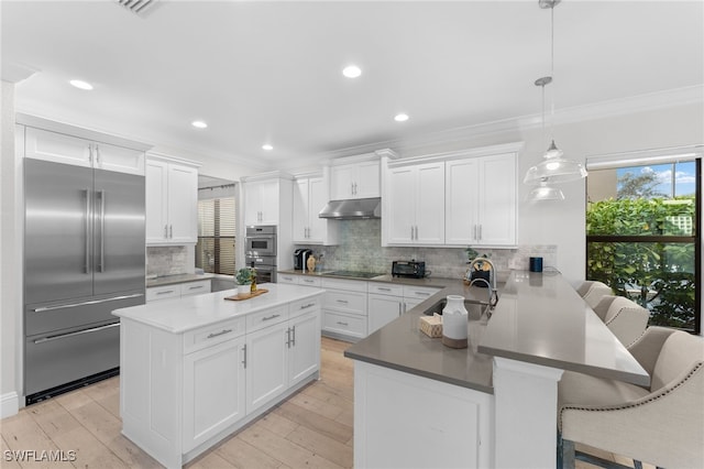 kitchen with a breakfast bar, sink, appliances with stainless steel finishes, decorative light fixtures, and kitchen peninsula