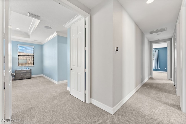 corridor with a raised ceiling, ornamental molding, and light carpet