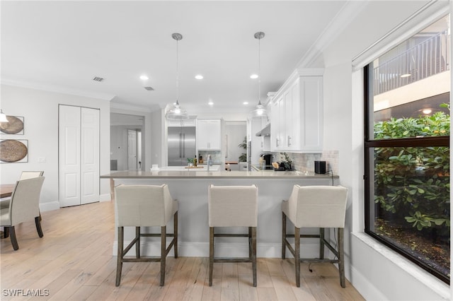 kitchen featuring tasteful backsplash, decorative light fixtures, white cabinets, built in refrigerator, and a breakfast bar area