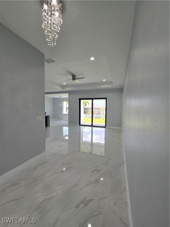 empty room with ceiling fan with notable chandelier and a tray ceiling