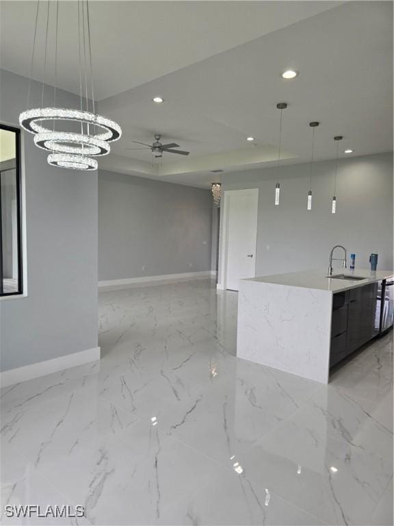 kitchen with a tray ceiling, sink, ceiling fan with notable chandelier, and decorative light fixtures