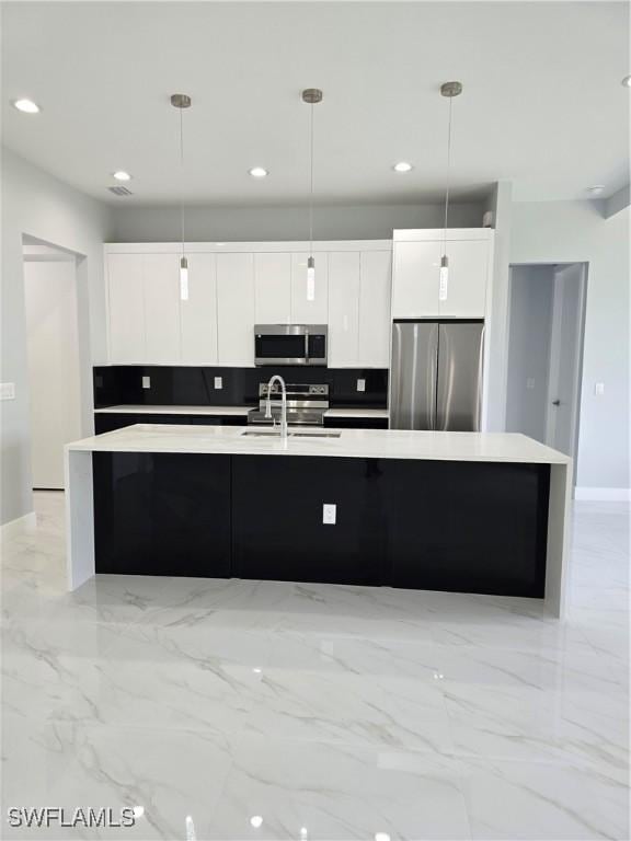 kitchen featuring appliances with stainless steel finishes, a kitchen island with sink, sink, white cabinets, and hanging light fixtures