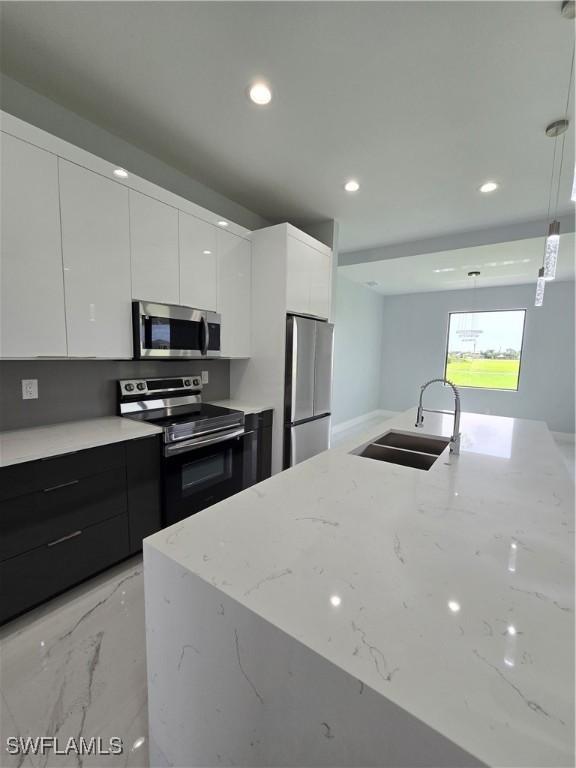 kitchen with light stone countertops, stainless steel appliances, sink, decorative light fixtures, and white cabinetry