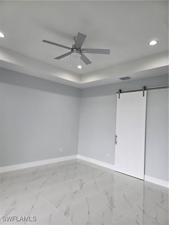 empty room with ceiling fan, a barn door, and a tray ceiling