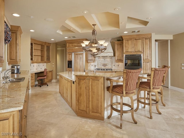 kitchen with a center island, black oven, light stone counters, sink, and tasteful backsplash