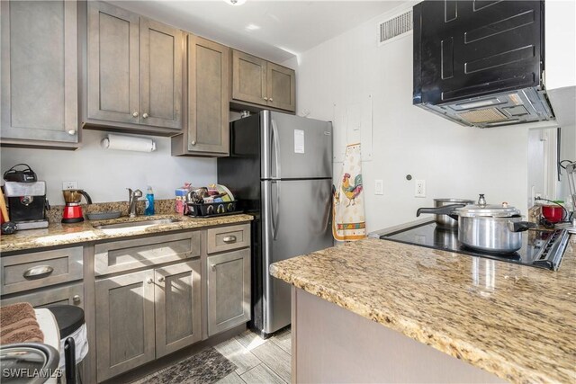 kitchen with light stone counters, black electric cooktop, stainless steel refrigerator, and sink