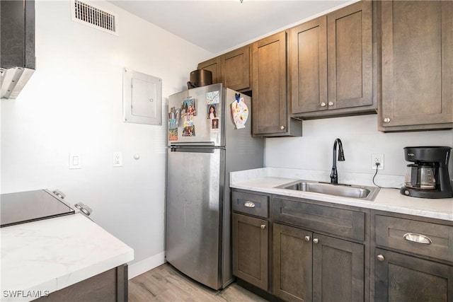 kitchen featuring electric panel, sink, light hardwood / wood-style flooring, stainless steel fridge, and dark brown cabinetry