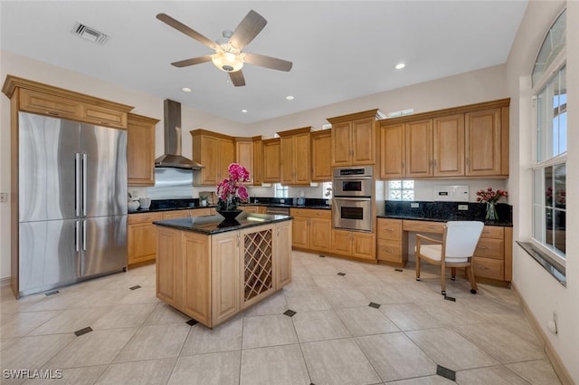 kitchen with light tile patterned flooring, wall chimney exhaust hood, a center island, dark stone counters, and stainless steel appliances