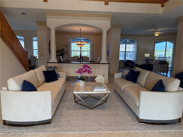 tiled living room featuring ornamental molding, ceiling fan with notable chandelier, and decorative columns