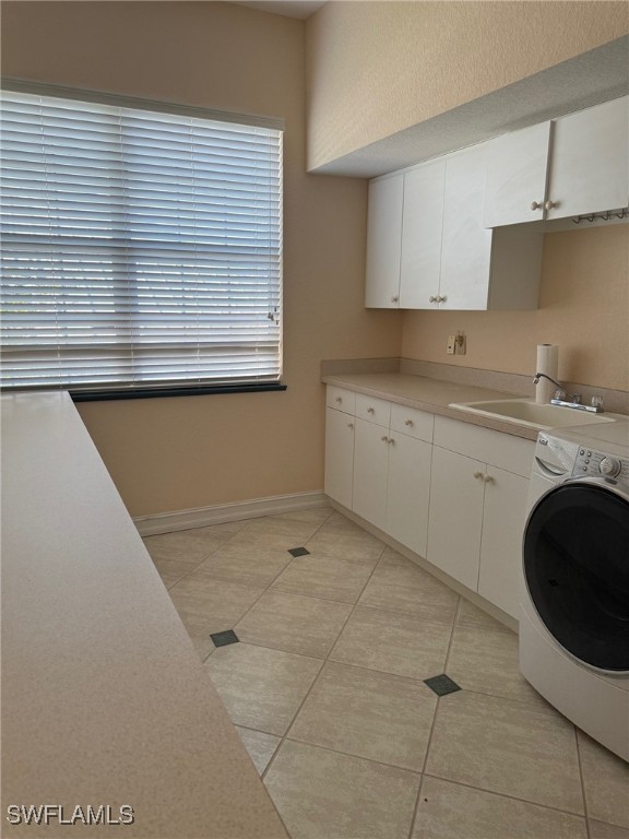 clothes washing area featuring sink, light tile patterned floors, washer / dryer, and cabinets