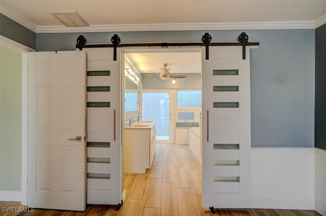 corridor with light hardwood / wood-style floors, sink, crown molding, and a barn door