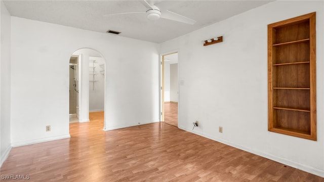 empty room featuring light wood-type flooring, built in features, and ceiling fan