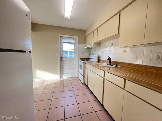 kitchen with refrigerator, light tile patterned floors, backsplash, white range with electric cooktop, and sink