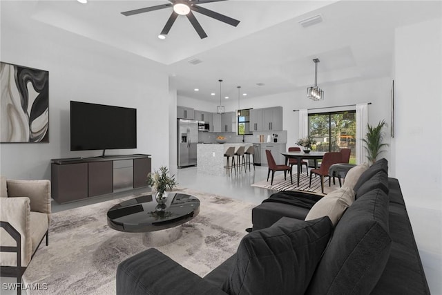 living room with ceiling fan with notable chandelier and a raised ceiling