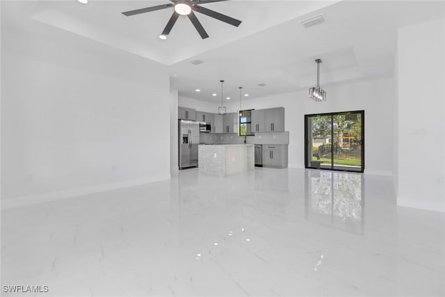 unfurnished living room with ceiling fan and a tray ceiling