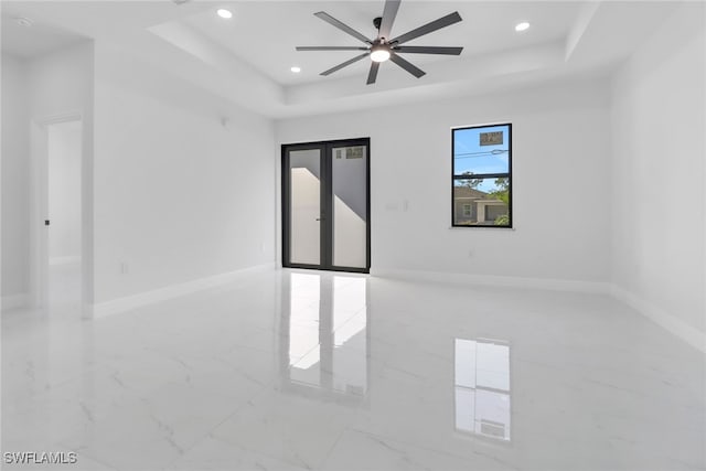 empty room with ceiling fan, a raised ceiling, and french doors