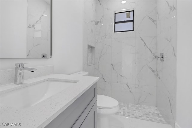 bathroom with a tile shower, vanity, and toilet