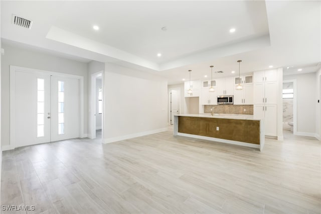 unfurnished living room with french doors, light hardwood / wood-style floors, a raised ceiling, and sink