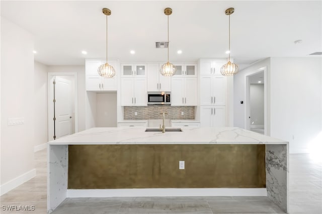 kitchen featuring sink, pendant lighting, light stone counters, and an island with sink