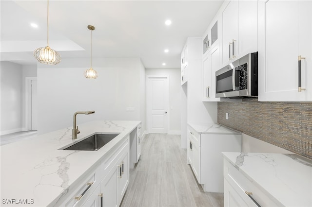 kitchen with light stone countertops, appliances with stainless steel finishes, sink, decorative light fixtures, and white cabinetry