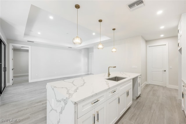 kitchen featuring white cabinets, light stone counters, sink, and a tray ceiling