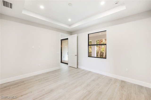 empty room featuring a tray ceiling and light hardwood / wood-style flooring