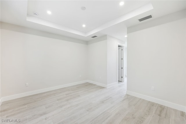 empty room with light wood-type flooring and a raised ceiling