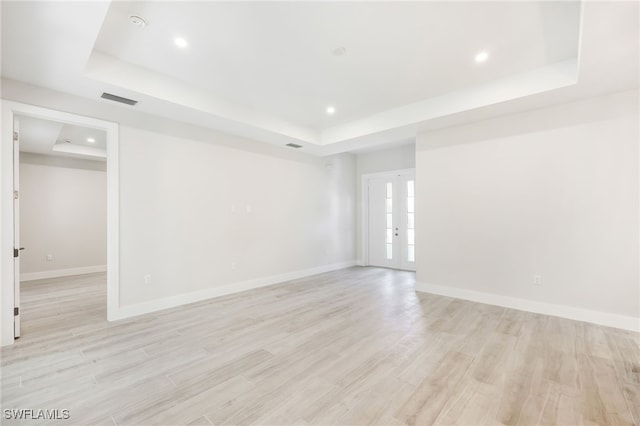 spare room with a tray ceiling and light hardwood / wood-style floors