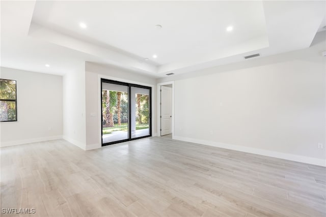 spare room featuring a raised ceiling and light hardwood / wood-style floors