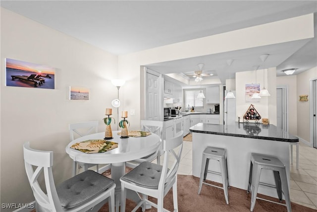 tiled dining space with a tray ceiling and ceiling fan