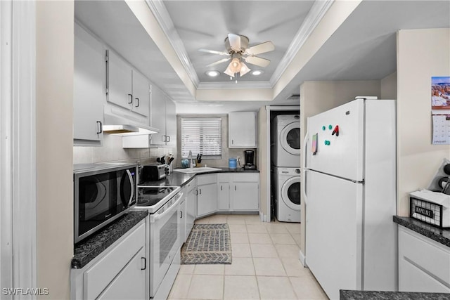 kitchen with stacked washing maching and dryer, white appliances, a raised ceiling, white cabinetry, and light tile patterned flooring