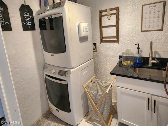 laundry area featuring a sink, stacked washer and dryer, cabinet space, and a textured wall