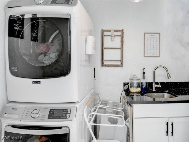 laundry room featuring a sink, cabinet space, stacked washer / drying machine, and a textured wall