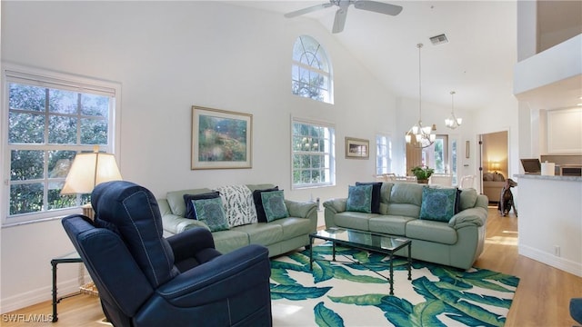 living room with ceiling fan with notable chandelier, light hardwood / wood-style floors, and a towering ceiling