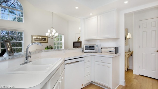 kitchen with white dishwasher, sink, light hardwood / wood-style flooring, an inviting chandelier, and white cabinetry