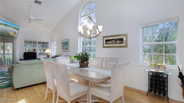 dining space with light wood-type flooring, ceiling fan with notable chandelier, and high vaulted ceiling