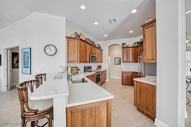 kitchen with sink, kitchen peninsula, a breakfast bar area, light tile patterned floors, and appliances with stainless steel finishes