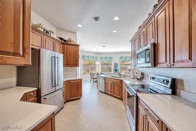 kitchen with appliances with stainless steel finishes, light stone counters, sink, light tile patterned floors, and pendant lighting