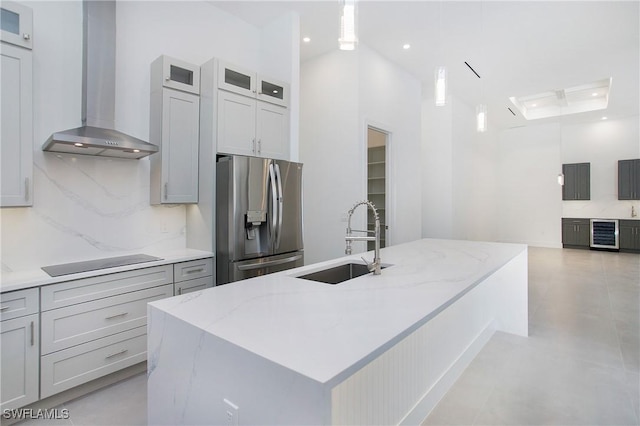 kitchen featuring light stone countertops, sink, wall chimney exhaust hood, stainless steel fridge, and a kitchen island with sink