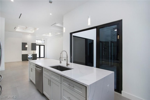 kitchen with light stone countertops, sink, dishwasher, hanging light fixtures, and an island with sink