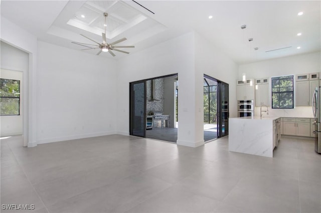 unfurnished living room with ceiling fan, sink, a high ceiling, and coffered ceiling